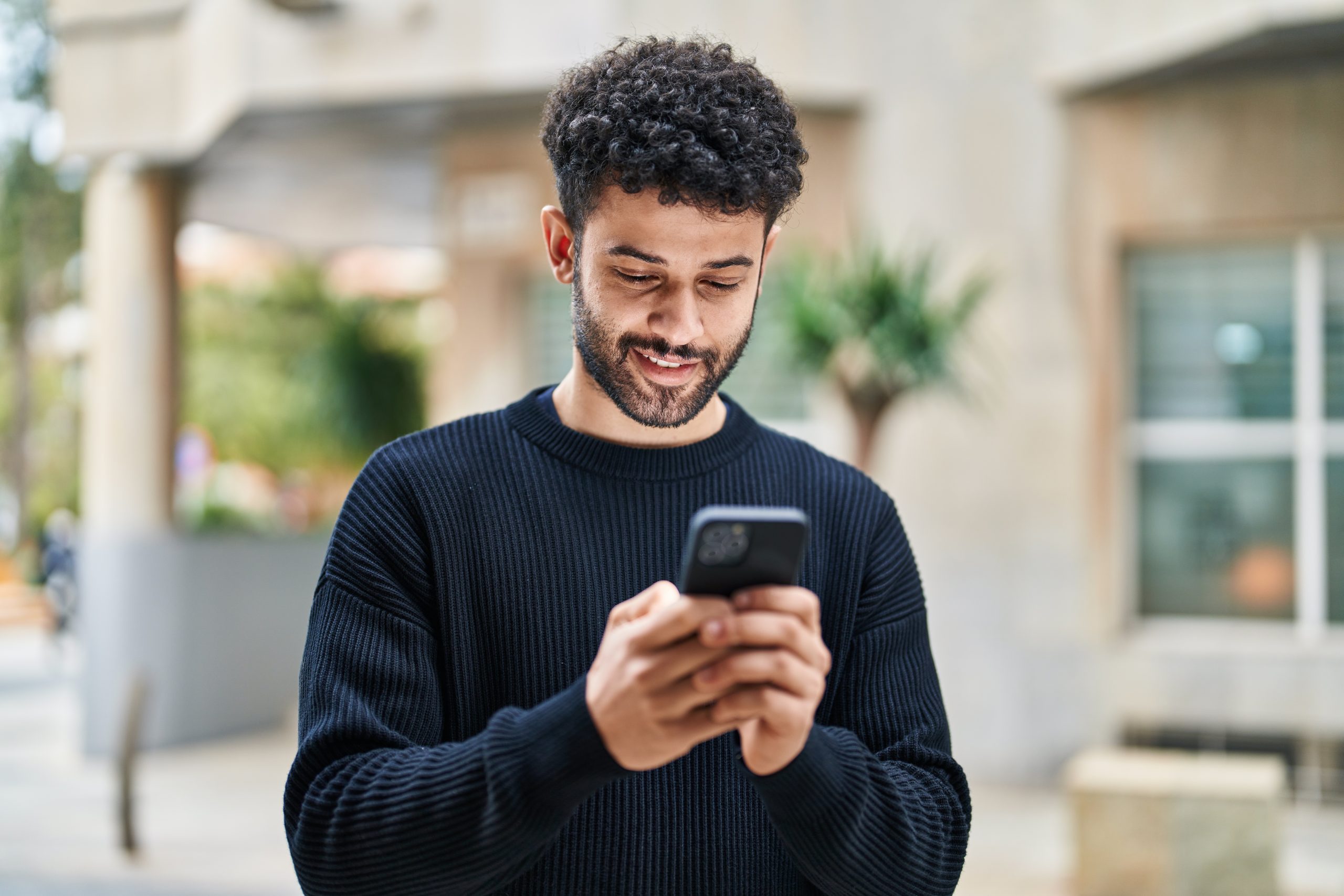 Young man outdoors looking at his phone and smiling